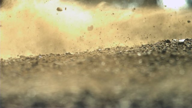 Dirt and rocks blowing across a path in slow motion with sun