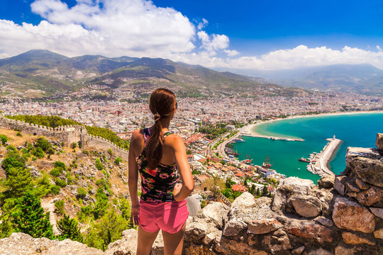 Woman look on landscape of Alanya with marina and Kizil Kule red tower in Antalya district, Turkey, Asia. Famous tourist destination with high mountains. Summer bright day and sea shore