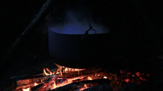 Cooking in cauldron over the open fire in the dark. Boiling food outdoors.