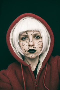 Retrato de una mujer joven con el pelo blanco y capucha con interrogaciones pintadas en su cara 