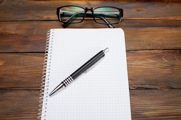 Fototapeta premium Notepad in box with white pages, glass spectacles in black frame and pen on wooden background. Top view