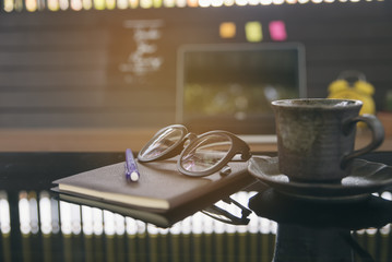 Business,coffee shop or student desk concept.A wooden desk with a laptop, notebook,glasses,pen,notebook and cup of coffee in morning,working space.