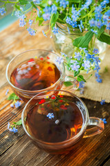 Tea cup, teapot, honey jar and summer bouquet of blue cornflowers on table outdoors. Summer still life.