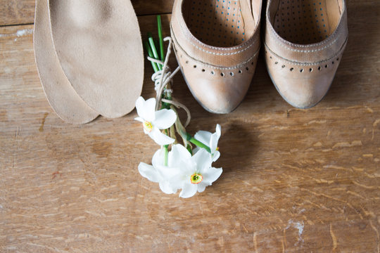 Beige leather shoes with orthopedic insoles and  white daffodils. Wooden background.