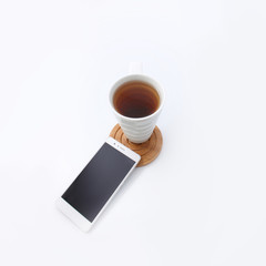 Fototapeta na wymiar White cup with tea on wooden round pillar with white phone on white background