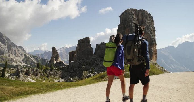 Man and woman couple hiking along Cinque Torri trail path. Group of friends summer adventure journey in mountain nature outdoors. Travel exploring Alps, Dolomites, Italy. 4k slow motion 60p video