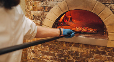 Restaurant chef takes pizza from oven in traditional restaurant.