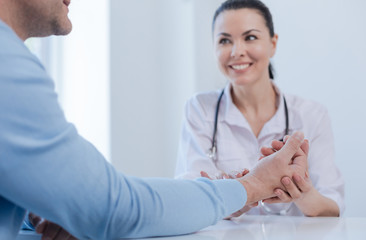 Cheerful practitioner checking patient pulse indoors