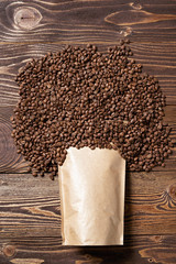 Mock-up craft paper pouch bag top view over wooden background with coffee beans over