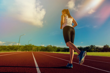 Sporty woman running on stadium track in evening focus on sport wear, shoes and legs. Fitness and workout wellness concept.