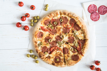 top view of homemade italian pizza with sausages, cherry tomatoes and olives on wooden surface