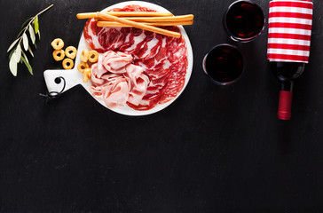 Cold meat cut from different varieties of salami on a dark background with a bottle of red wine and...