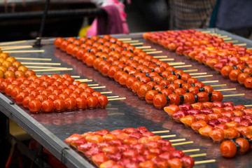 Fruit candy look so bright and vivid and delicious selling by street vendor. Tomato, strawberry, coated with sugar. Sugary dessert shop on the street. 