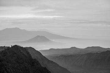 Black and white landscape photo of mountains in the fog and cloud during foggy and misty morning while cold breezy air blowing above all the mountains. 