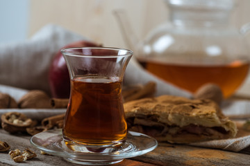 hot tea in glass cup and homemade apple pie with walnuts on rustic wooden tabletop