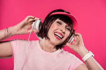 Fototapeta premium portrait of cheerful senior woman listening music in headphones isolated on pink