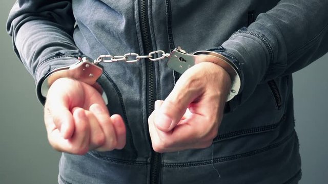 Arrested computer hacker and cyber criminal with handcuffs, close up of hands