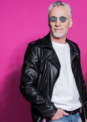 Portrait of stylish handsome senior man in leather jacket and sunglasses posing with hand in pocket