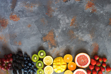 Top view of rainbow colored fruits on the grey stone background, copy space for text, selective focus