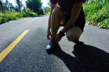 Young fitness woman tying shoelace on morning tropical forest trail
