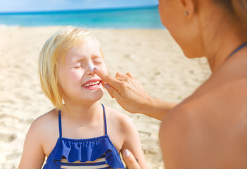 happy young mother and daughter on beach applying SPF