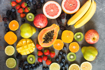Different rainbow colored fruits, strawberries, blueberries, mango, orange, grapefruit, banana, apple, grapes, kiwis on the grey background, above view, selective focus