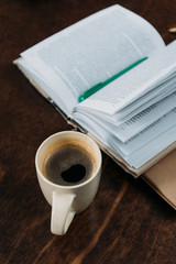 close up of coffee cup with book and pen on wooden tabletop