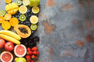 Top view of rainbow colored fruits and berries on the grey stone background, copy space for text, selective focus