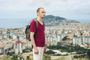 Man traveler with backpack explores the city looking at the panoramic view of the city and the coast.