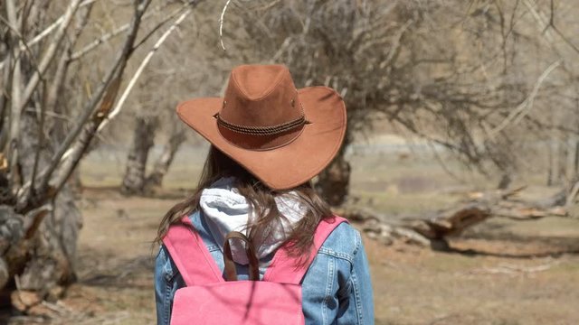 Young traveler female in a broad-brimmed hat and pink backpack admires the forest, looks around close-up 4k.