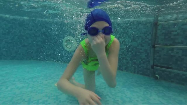 Joyful child swims in the pool under water clamping the nose with his hand. Slow motion