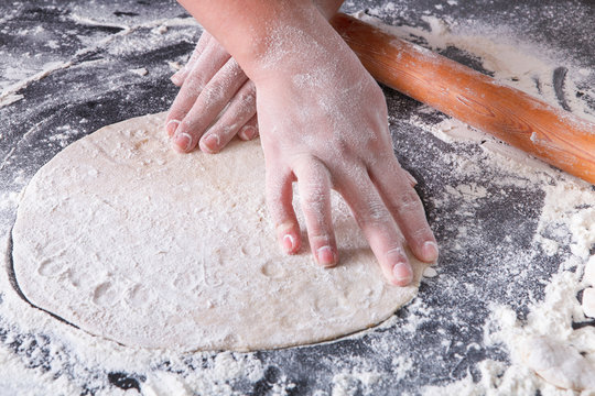 Baking concept. Hands roll dough on black background.
