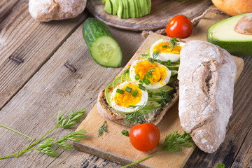 Avocado and egg sandwich on a wooden background. Fresh organic vegetables, eggs and whole wheat bread. Healthy breakfast. Rustic style.