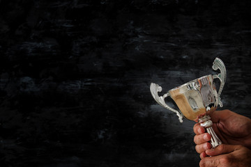 low key image of a man holding a trophy cup over dark background.