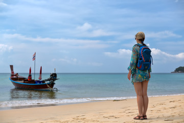 girl with a backpack on the beach, traditional Thai boat