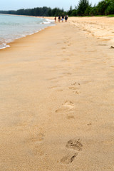 Traces of feet in the sand, a group of people in the distance.
