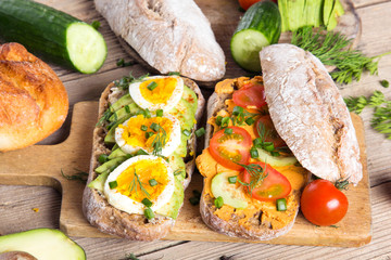 Sandwiches with avocado, eggs and tomato on a wooden background. Fresh organic vegetables, eggs and whole wheat bread. Healthy breakfast. Retro style.