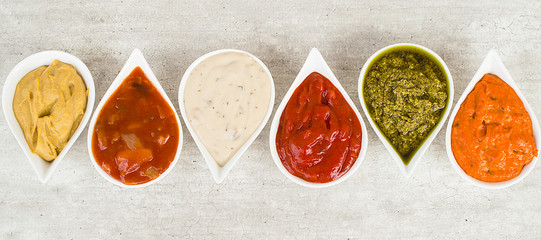 Top view on a set of sauces on a light gray stone background.