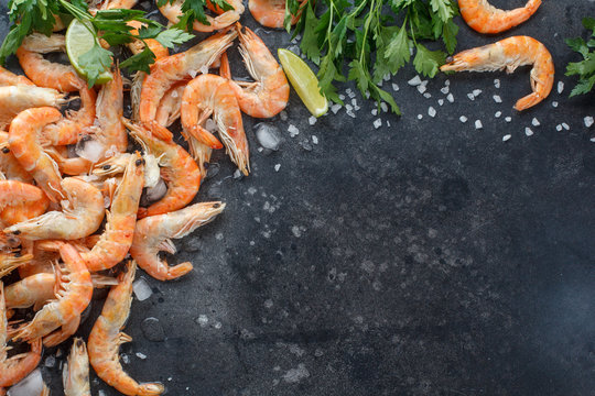 Shrimps with lime, ice, herbs and sea salt on a black background. Frame for your text. Shrimp with herbs and spices scattered on black background. Food background.