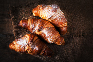 Fresh croissants on a table close up. Tasty golden croissants on dark brown  wooden background macro
