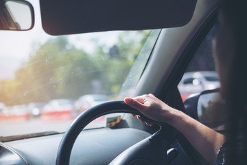 Woman holding on black steering wheel while driving a car with traffic background