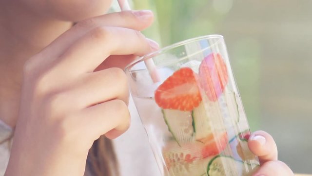 Young woman drinking cucumber and strawberry detox water .