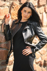 Portrait of young pretty white girl with black hair and in black clothes posing near the old stone wall.