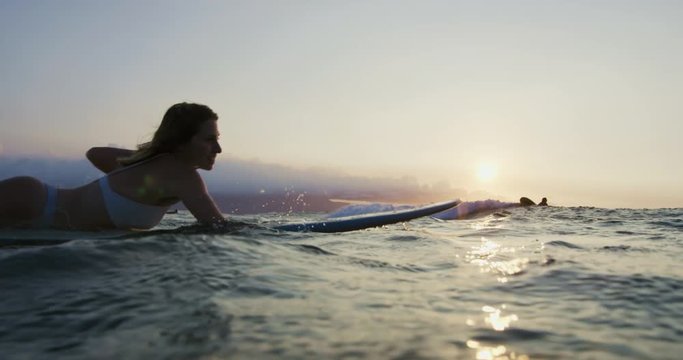 Beautiful young woman surfing in bikini at sunset in slow motion