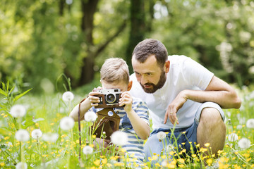 Young father with little boy with camera in summer park.