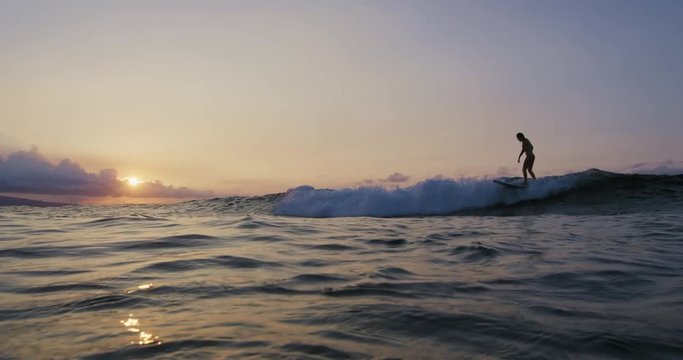 Beautiful young woman surfing in bikini at sunset in slow motion