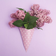 Bunch of lilac flowers in paper cone on purple background from above, flat lay