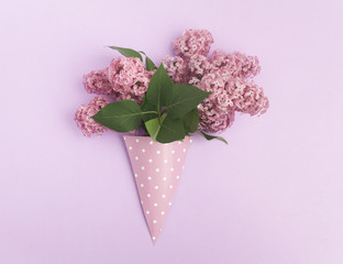 Bunch of lilac flowers in paper cone on purple background from above, flat lay