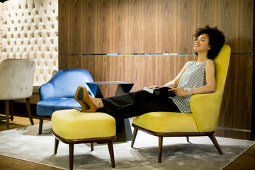Young woman sittinh on a yellow chair and reading a book