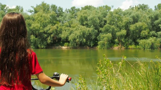 Girl on a red bicycle by the river. Child with a bicycle in nature.